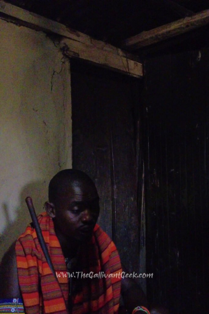 Maasai man sitting inside a small, dark traditional house