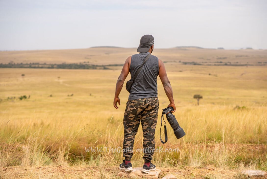 Wildlife photographer standing in the Masai Mara grasslands holding a Sony camera with a telephoto lens