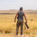 Wildlife photographer standing in the Masai Mara grasslands holding a Sony camera with a telephoto lens