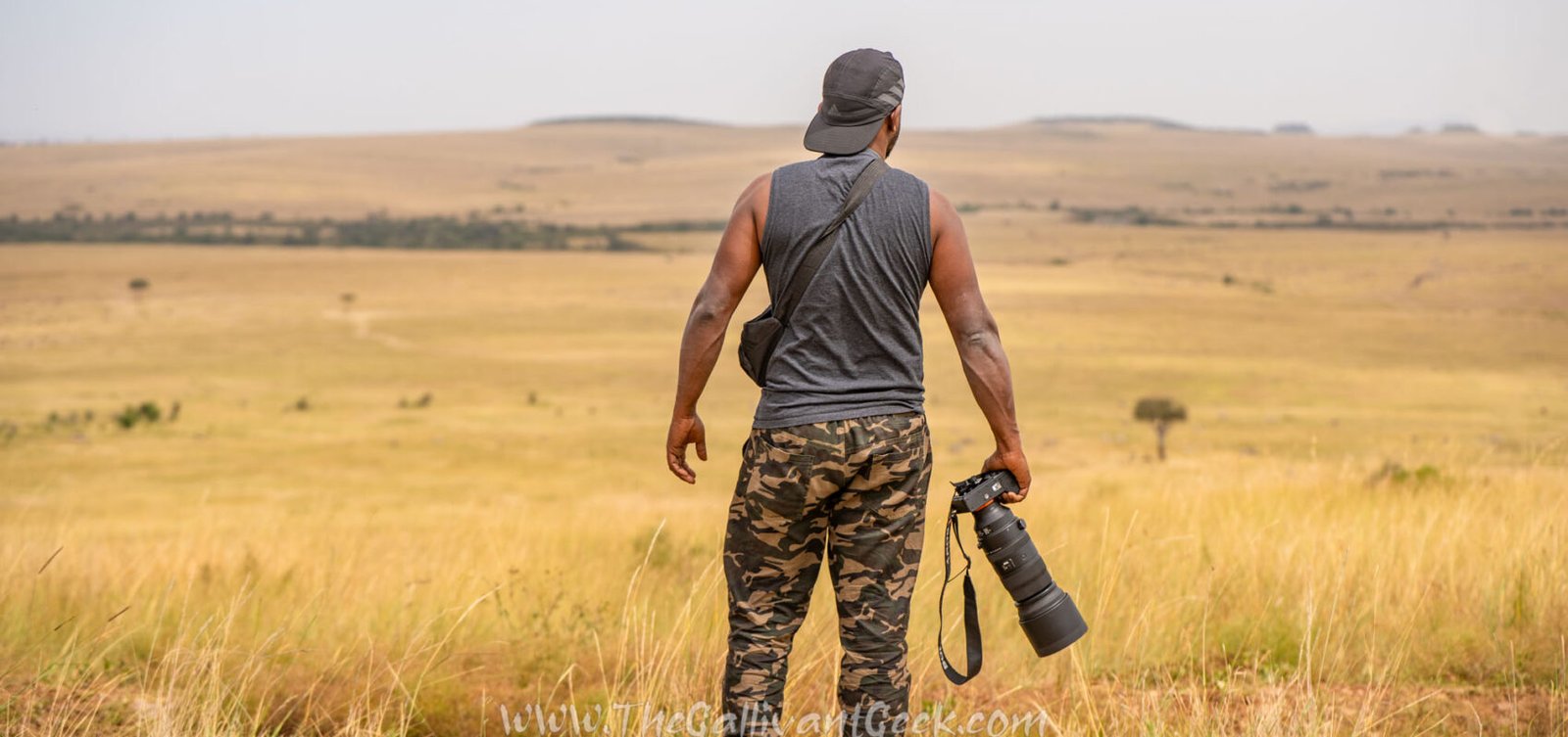 Wildlife photographer standing in the Masai Mara grasslands holding a Sony camera with a telephoto lens
