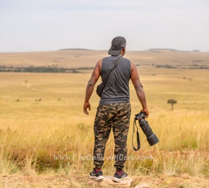 Wildlife photographer standing in the Masai Mara grasslands holding a Sony camera with a telephoto lens