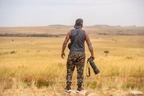 Wildlife photographer standing in the Masai Mara grasslands holding a Sony camera with a telephoto lens