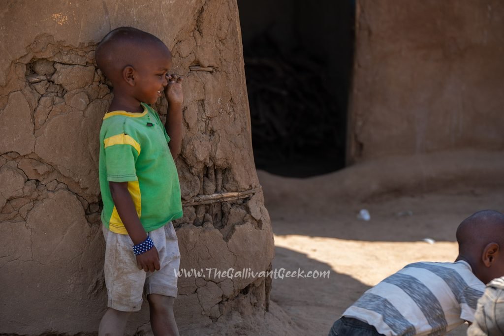 Maasai child in a green shirt outside a mud house