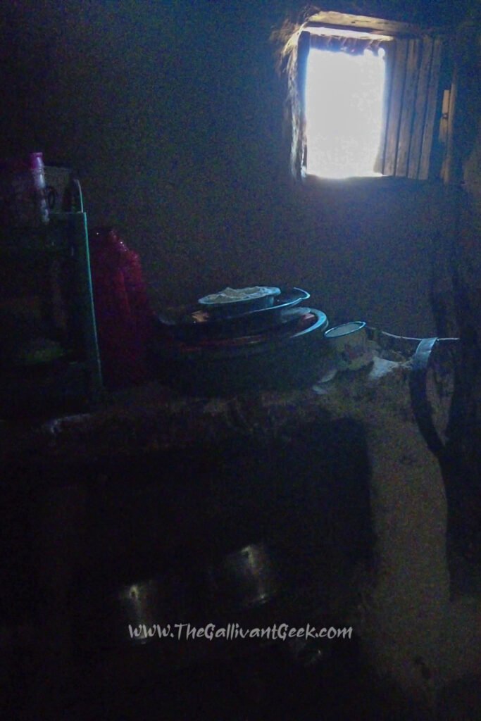Small kitchen inside a dark traditional Maasai house, lit by a small window