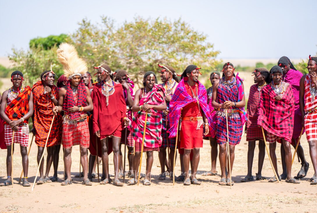 Maasai men and women in red shukas lined up to welcome visitors in a Maasai village in the Masai Mara