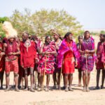 Maasai men and women in red shukas lined up to welcome visitors in a Maasai village in the Masai Mara