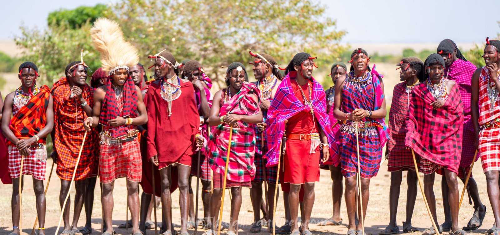 Maasai men and women in red shukas lined up to welcome visitors in a Maasai village in the Masai Mara