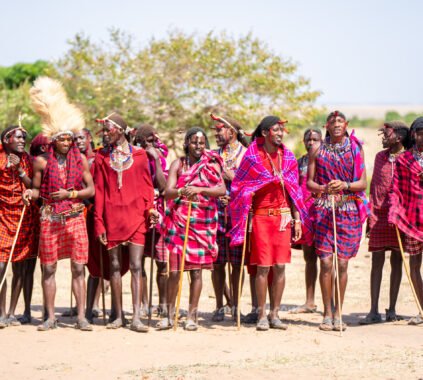 Maasai men and women in red shukas lined up to welcome visitors in a Maasai village in the Masai Mara