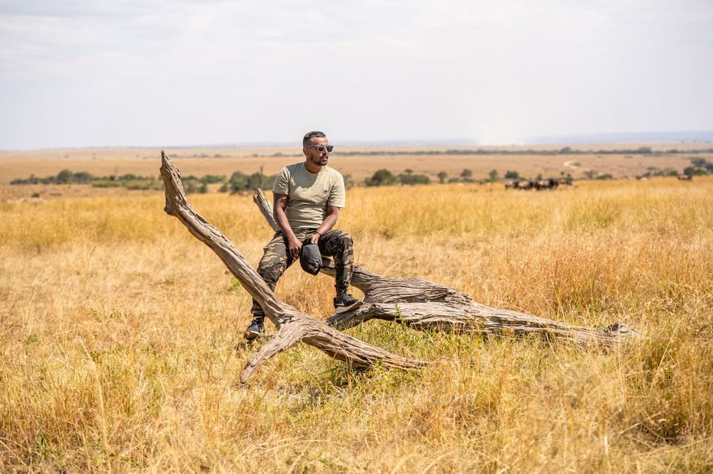 Wildlife photographer Shakir sitting on a fallen tree in the Masai Mara grasslands